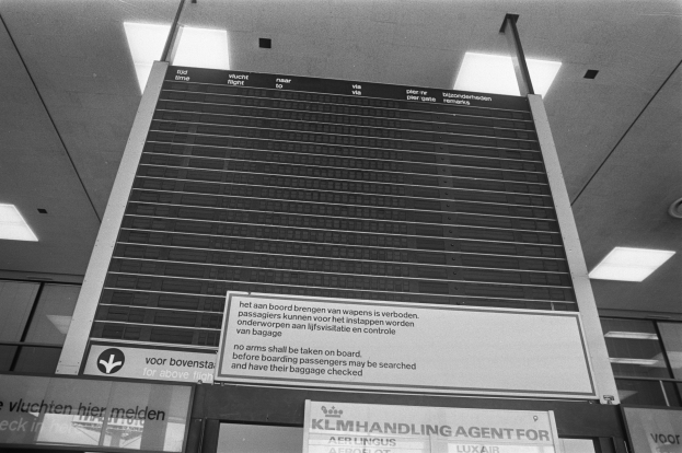 Ein Schwarz-Weiß-Foto eines Abflugsbildschirms an der Decke befestigt, mit Leuchten, die den Bereich beleuchten.