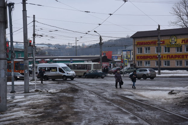 Eine Gruppe von Menschen, die neben einer Bahnschiene auf einer Straße mit Fahrzeugen, Strommasten, Ampeln, Gebäuden, Bäumen und einem Van gehen.