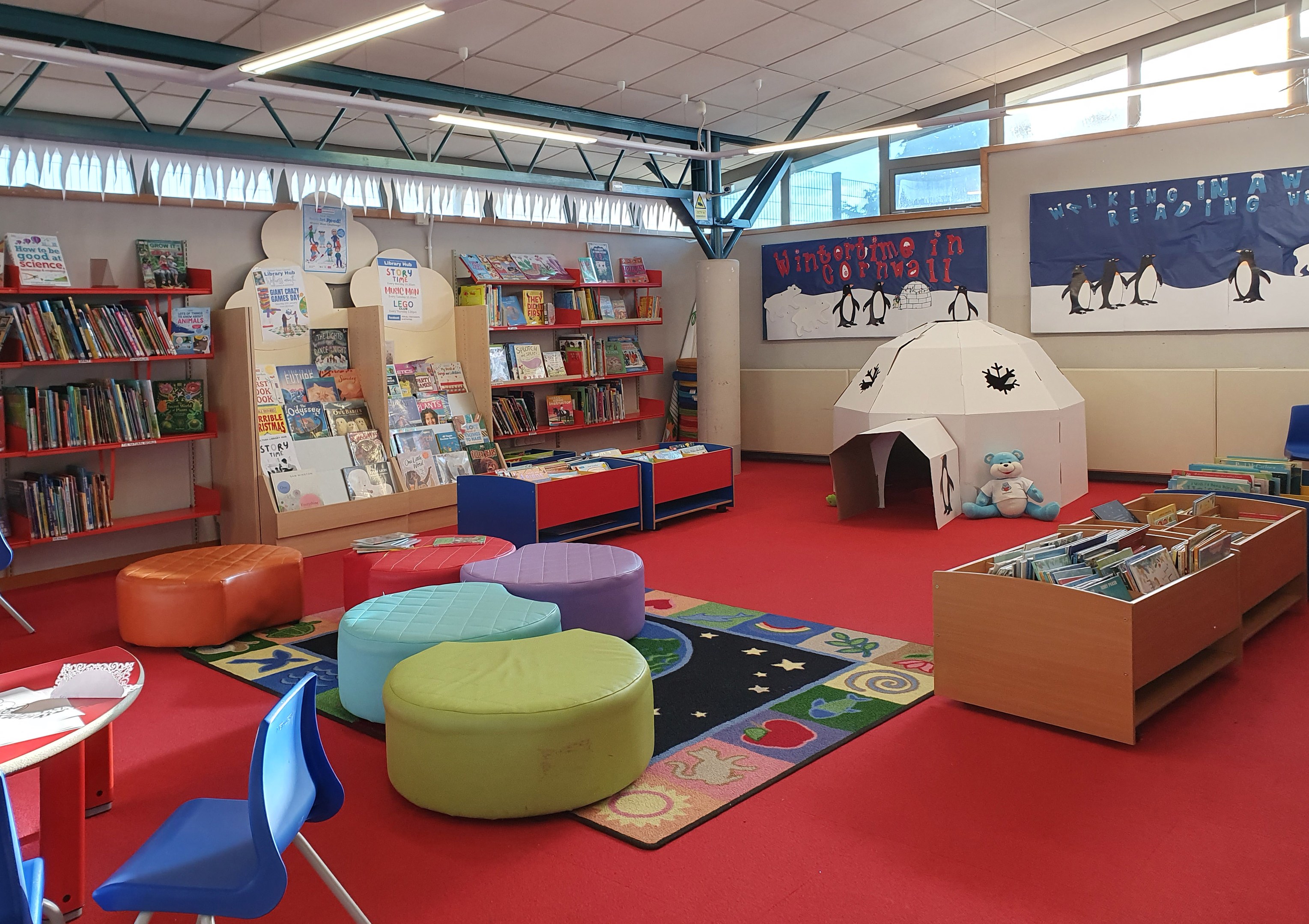 Ein Kinderbibliotheksraum mit Bücherregalen, Möbeln, Lehrtafeln an den Wänden, Deckenlampen und Glasfenstern.