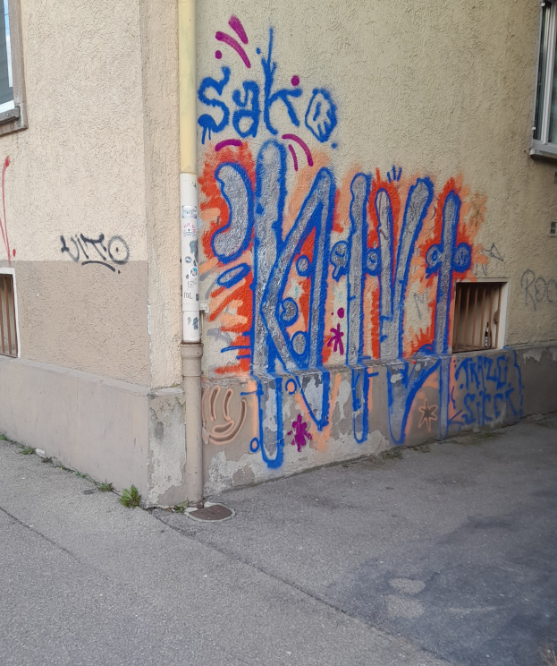 Gebäude mit Fenstern, einem Rohr und Graffiti an der Seite, das über einer Straße liegt.