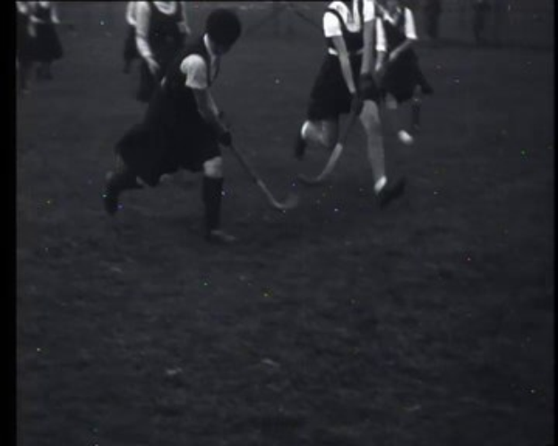 Schwarzes und weißes Foto einer Gruppe junger Mädchen, die auf einem Feld Hockey spielen, jede hält einen Hockey-Schläger in der Hand.