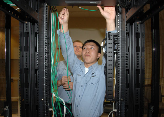 Zwei Männer arbeiten an einem Server in einem Rechenzentrum mit Kabelregalen und einer Wand im Hintergrund.