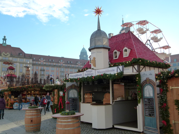 Ein geschäftiger Weihnachtsmarkt in Nürnberg, Deutschland, mit Menschen um geschmückte Stände, festlicher Beleuchtung, einem Riesenrad im Hintergrund und einer Tafel auf der rechten Seite.