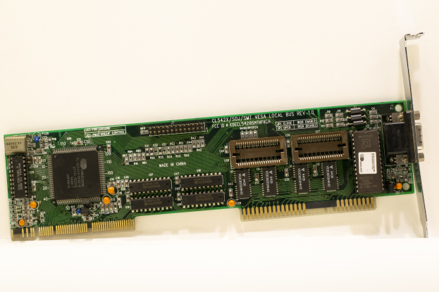 Nahaufnahme einer PCI-E-Karte mit einem zentralen Chip und mehreren Verbindern auf einer weißen Oberfläche.