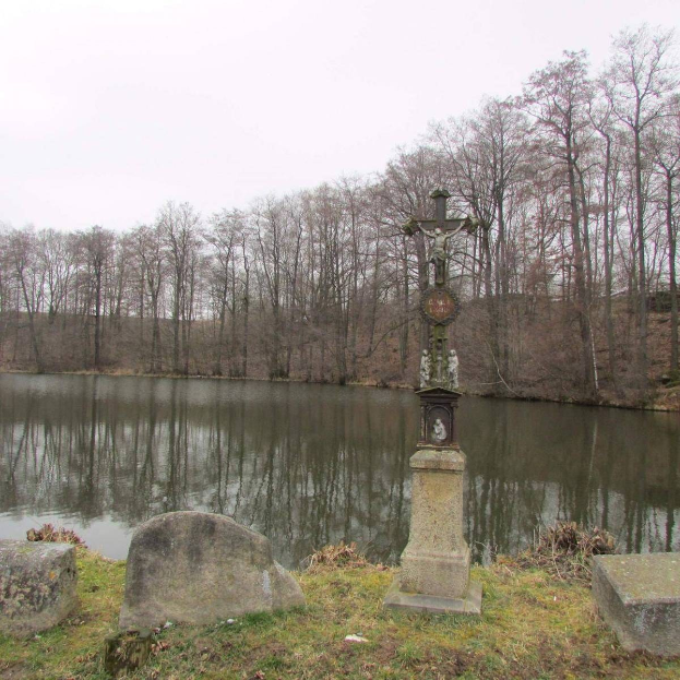 Ein Friedhof mit einem Kreuz in der Mitte eines Sees, umgeben von Bäumen, Grabsteinen und saftigem Grün unter einem sichtbaren Himmel.