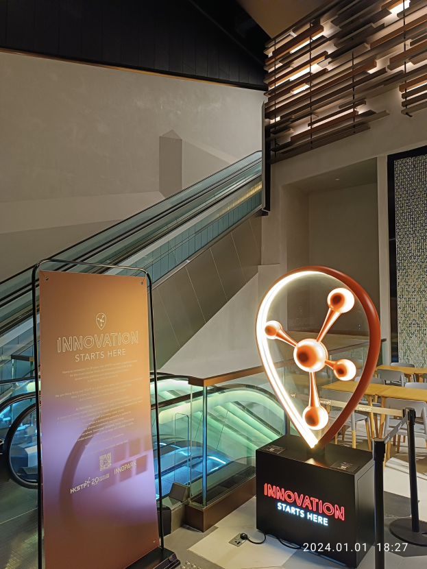 Großes Schild in einem Gebäude mit einer Rolltreppe im Hintergrund, mit Tischen und Stühlen auf der rechten Seite und einer Tafel mit "Innovation Starts Here" auf der linken Seite, die auf die HSTP20 Expo hinweist.