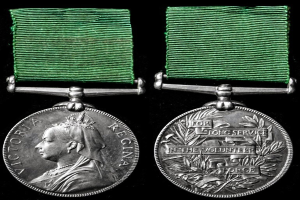 Zwei silberne Medaillen mit grünen Bändern auf schwarzem Hintergrund, eine mit einer Person und die andere mit eingravierter Schrift.