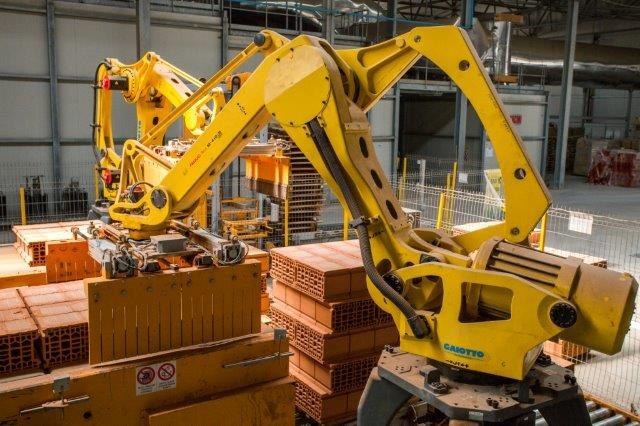 Großes Industriegebäude mit gestapelten Kisten, Kränen, Zaun, Strommasten und einer fernen Wand in einer Fertigungsumgebung.