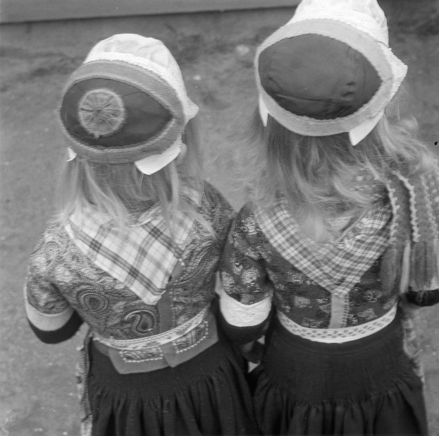 Zwei junge Mädchen in traditionellen bayerischen Trachten und Hüten stehen Seite an Seite vor einer Wand in einem Schwarz-Weiß-Foto.