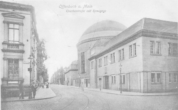 Schwarzes und weißes Foto einer Stadtstraße mit der Beschriftung "Offenbach a Main, Goethestraße mit Synagoge", das Gebäude, Laternenmasten, Lampen, Bäume und Fußgänger zeigt.