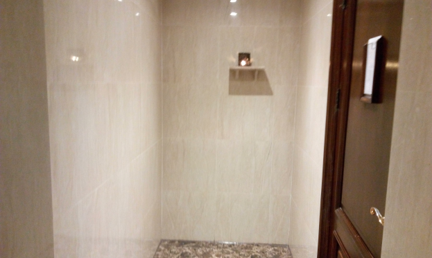 Badezimmer mit einer Duschkabine, Toilette und Tür auf der rechten Seite, mit Fliesen an den Wänden und Deckenleuchten.