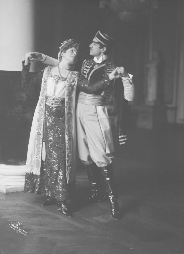 Schwarz-weißes Foto eines Mannes und einer Frau, die in einem Ballsaal tanzen, mit einer Säule und einer Wand im Hintergrund; der Mann trägt Tanzschuhe, was darauf hindeutet, dass sie mitten in einer Performance sind.