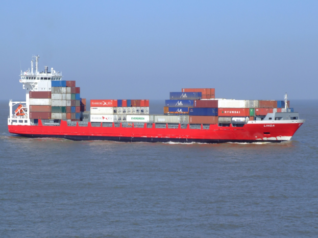 Großes rotes und weißes Containerschiff mit gestapelten Containern, das auf dem Meer unter einem klaren blauen Himmel segelt.