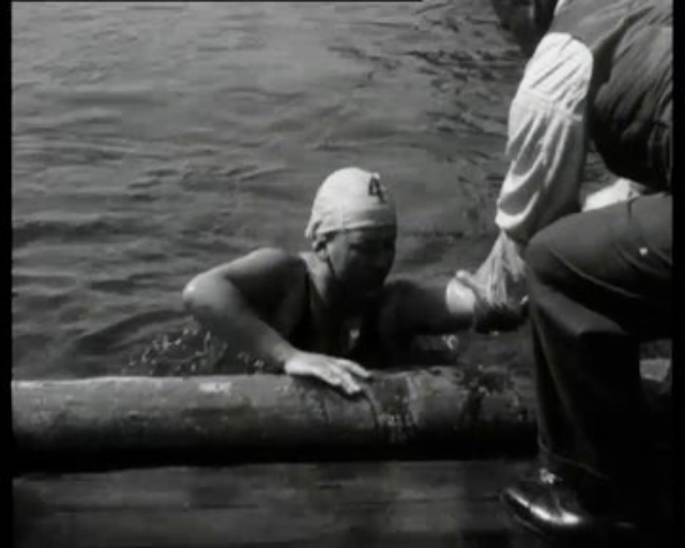 Ein Schwarz-Weiß-Bild eines Mannes in Not im Wasser mit einem Verband am Kopf, umgeben von zwei Personen rechts.