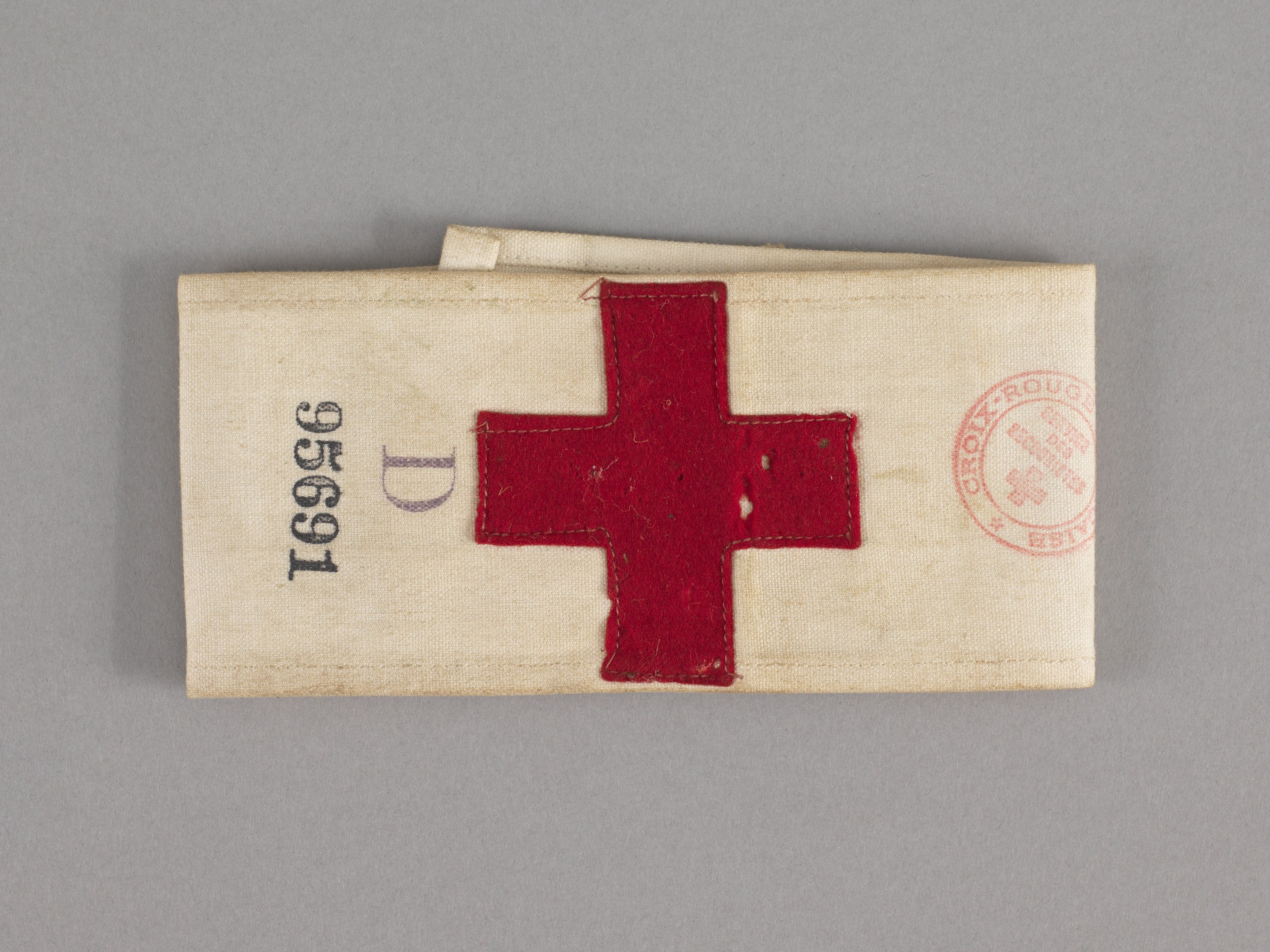 Ein rotes Kreuz-Ersthelfer-Set in einem Stoffbeutel mit Text und einem Stempel, das auf einer Oberfläche liegt.