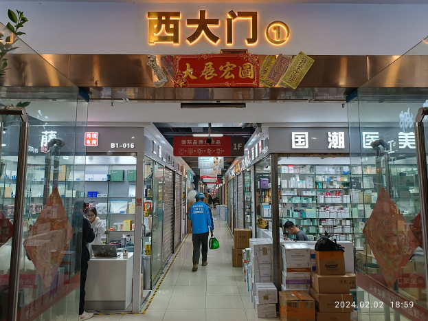 Innenansicht einer chinesischen Apotheke mit Glaswänden, Regalen voller Artikel, verstreuten Kartons auf dem Boden, einer Pflanze links und einem Namensschild oben, das darauf hinweist, dass es sich um eine chinesische Drogerie handelt.