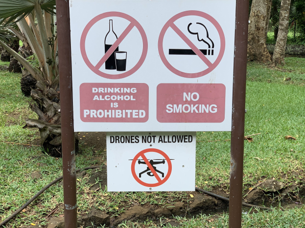 Straßenschilder, die das Trinken von Alkohol und Rauchen verbieten, mit Bäumen und Gras im Hintergrund.