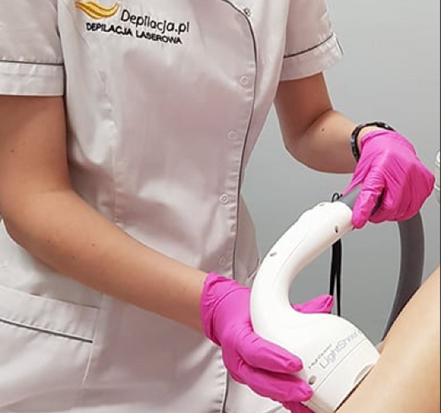 Eine Frau in einem weißen Hemd und pinken Handschuhen verwendet eine weiße Laser-Haarbehandlungsmaschine auf ihrer Haut, während sie vor einer Wand steht.