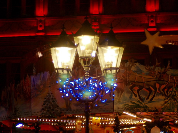 Eine mit Lichtern und Festtagsdekoration geschmückte Straßenlaterne, die in einer nächtlichen Stadt mit einem Gebäude im Hintergrund steht.