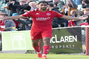 Ein Fußballspieler in roter Uniform rennt mit ausgestreckten Armen auf einem Feld, umgeben von Zuschauern hinter einem Zaun, mit einem Banner mit der Aufschrift 'Middlesbrough FC gegen Swansea City - Sky Bet Championship' im Vordergrund.