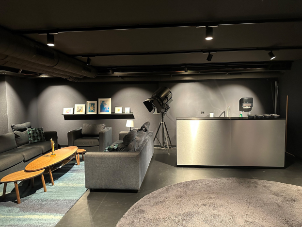 Ein Wohnzimmer mit Sofas, Tischen, einem Teppich, einer Spüle mit Wasserhahn, Fotorahmen an der Wand und Deckenlampen, Teil eines Medienstudios in London.