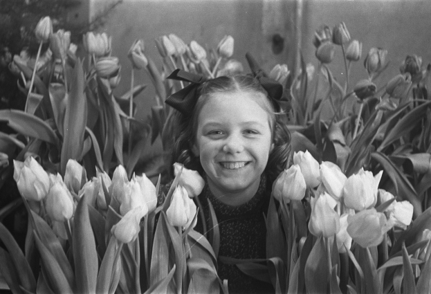 Ein junges Mädchen mit strahlendem Lächeln steht in einem Feld voller leuchtender Tulpen, das Schwarz-Weiß-Foto vermittelt einen zeitlosen Eindruck.