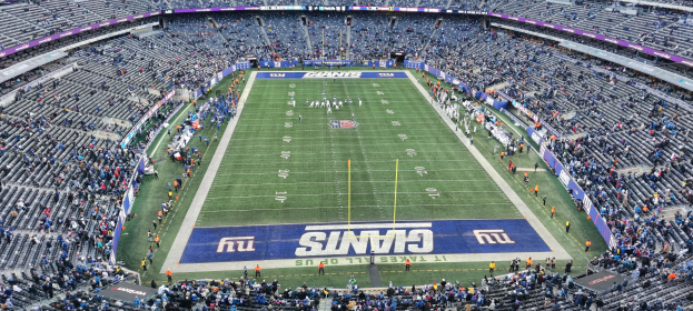 Ein volles Fußballstadion mit Spielern auf dem Feld, Torpfosten und Zuschauern auf den Sitzplätzen unter einer lebendigen Atmosphäre.
