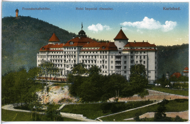 Alte Postkarte des Hotel Imperial in Karlsbad, Deutschland, das ein großes Gebäude mit Fenstern zeigt, umgeben von Bäumen, Pflanzen, Gras, einem Pfad, einer Baumgruppe, Hügeln und einem bewölkten Himmel, mit Text oben.