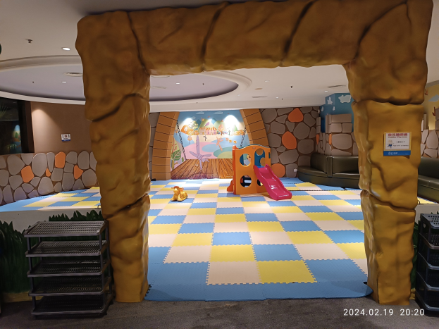 Kinderspielbereich mit einem zentralen Torbogen, verstreuten Spielzeugen, Ablagegestellen auf beiden Seiten, einer bemalten Wand im Hintergrund und Deckenbeleuchtung.