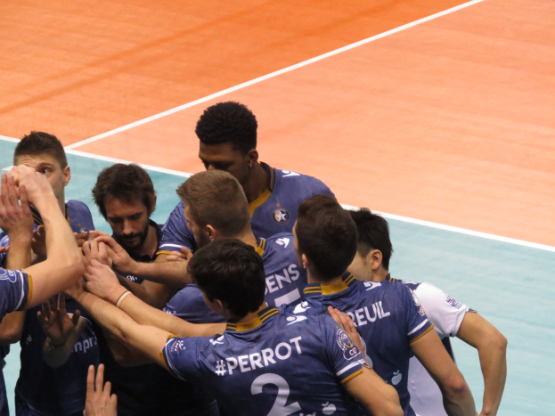 Eine Gruppe von Männern in blauen 'Ligue 1'-T-Shirts feiert auf einem Volleyballfeld.