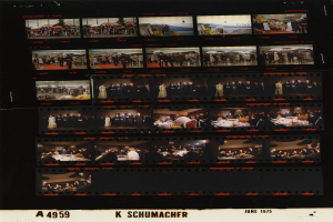 Schwarzes und weißes Foto einer vielseitigen Gruppe von Menschen in legerer Kleidung vor einem Filmstreifen mit "K Schumacher" darunter.