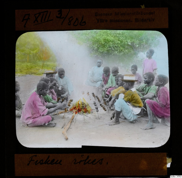 Eine Gruppe von Kindern sitzt um ein Feuer, einige tragen Hüte, mit Bäumen im Hintergrund und Textüberblattung.