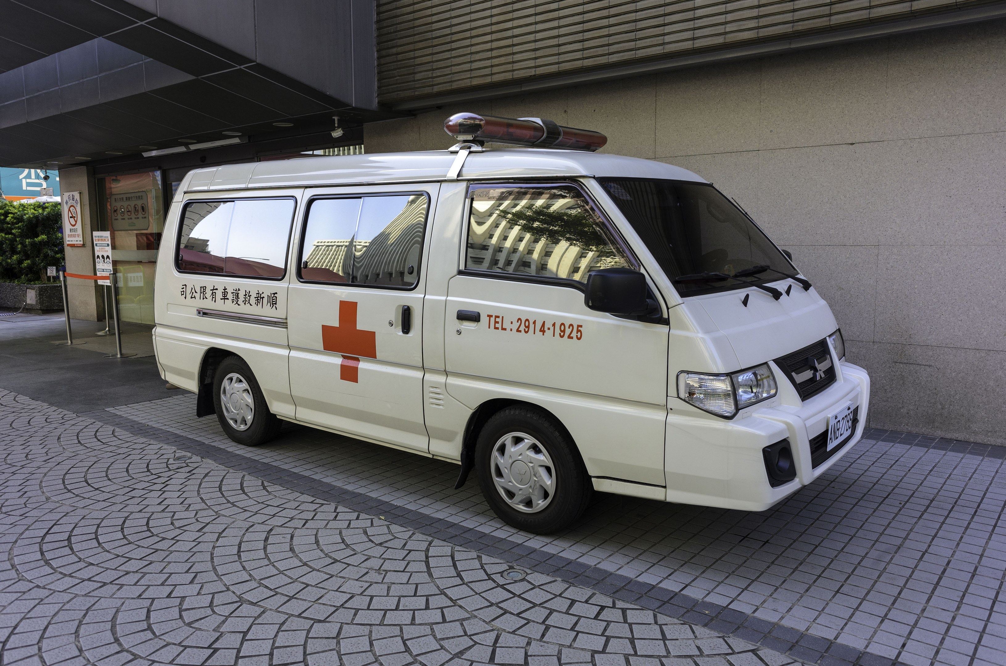 Notarztwagen vor einem Gebäude mit einem Schild, das darauf hinweist, dass es ein Notfahrzeug ist, umgeben von Bäumen und Pflanzen.