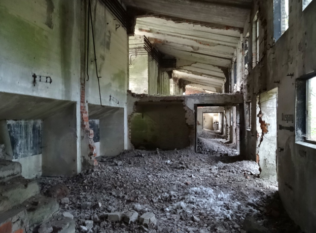 Altes Geb├Ąude mit erheblichen statischen Sch├Ąden, zerbrochene Fenster, verstreute Trümmern, freiliegende Rohre und Schutt, die einen schweren Verfall anzeigen.