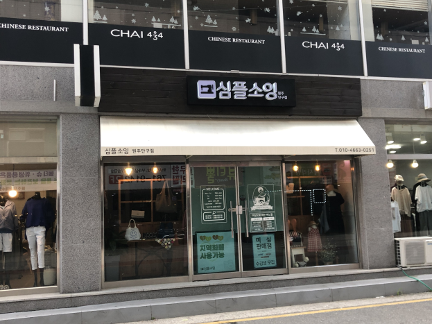 Außensicht des Chai 434 Chinesischen Restaurants in Seoul, Südkorea, mit Glaswänden, Schaufensterpuppen in Kleidern, beleuchteter Beschriftung, einer Klimaanlage auf der rechten Seite und einer Straße unten.