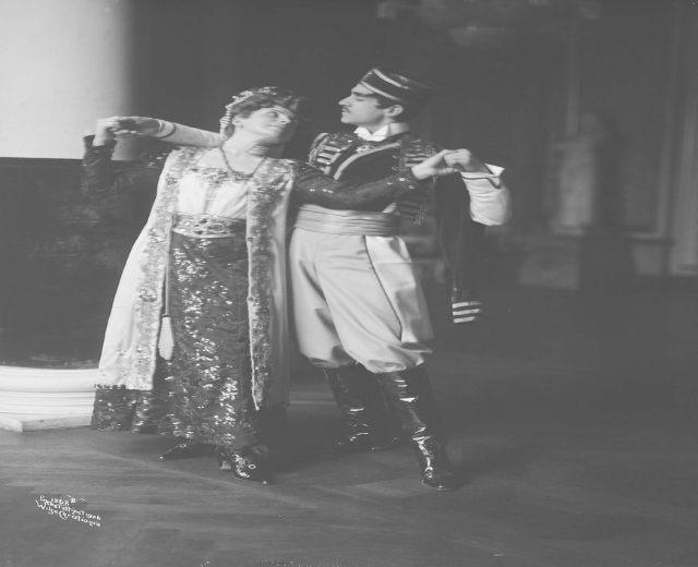 Schwarzes und weißes Foto eines Mannes und einer Frau, die in einem Ballsaal tanzen, mit einer Säule und einer Wand im Hintergrund; der Mann trägt Schuhe, was darauf hindeutet, dass sie performen.