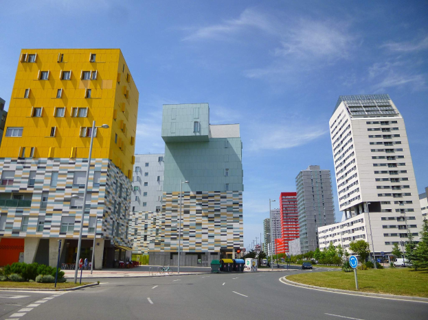 Eine Straße in der Stadt mit hohen Gebäuden, die als Teil der Universität Rotterdam gekennzeichnet sind, Straßenmäste, Straßenlaternen, Kraftfahrzeuge, Informationsschilder, Sträucher, Bäume und ein bewölkter Himmel.