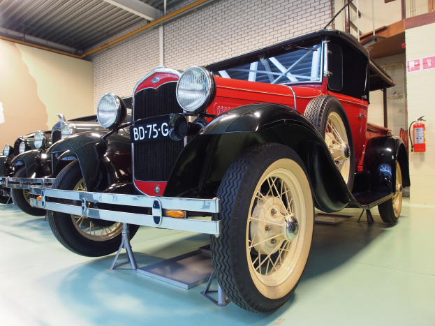 Eine Reihe von Oldtimern aus den 1930er Jahren, die in einem Museum ausgestellt sind, mit einem Feuerlöscher auf der rechten Seite und Deckenlampen darüber.