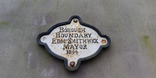 Metallschild an der Seite eines Gebäudes, das die Borough-Grenze markiert, mit "Edm Smithwick Mayor" in fetten weißen Buchstaben auf einem schwarzen Hintergrund.