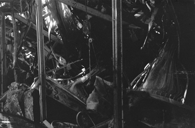 Schwarzes und weißes Foto eines feuerbeschädigten Gebäudes mit verstreuten Metallstangen und Trümmern.