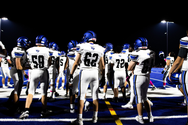 Eine Gruppe von Fussballspielern in Helmen und Stiefeln steht auf einem Feld unter Flutlicht und sieht bereit für ein Spiel aus.