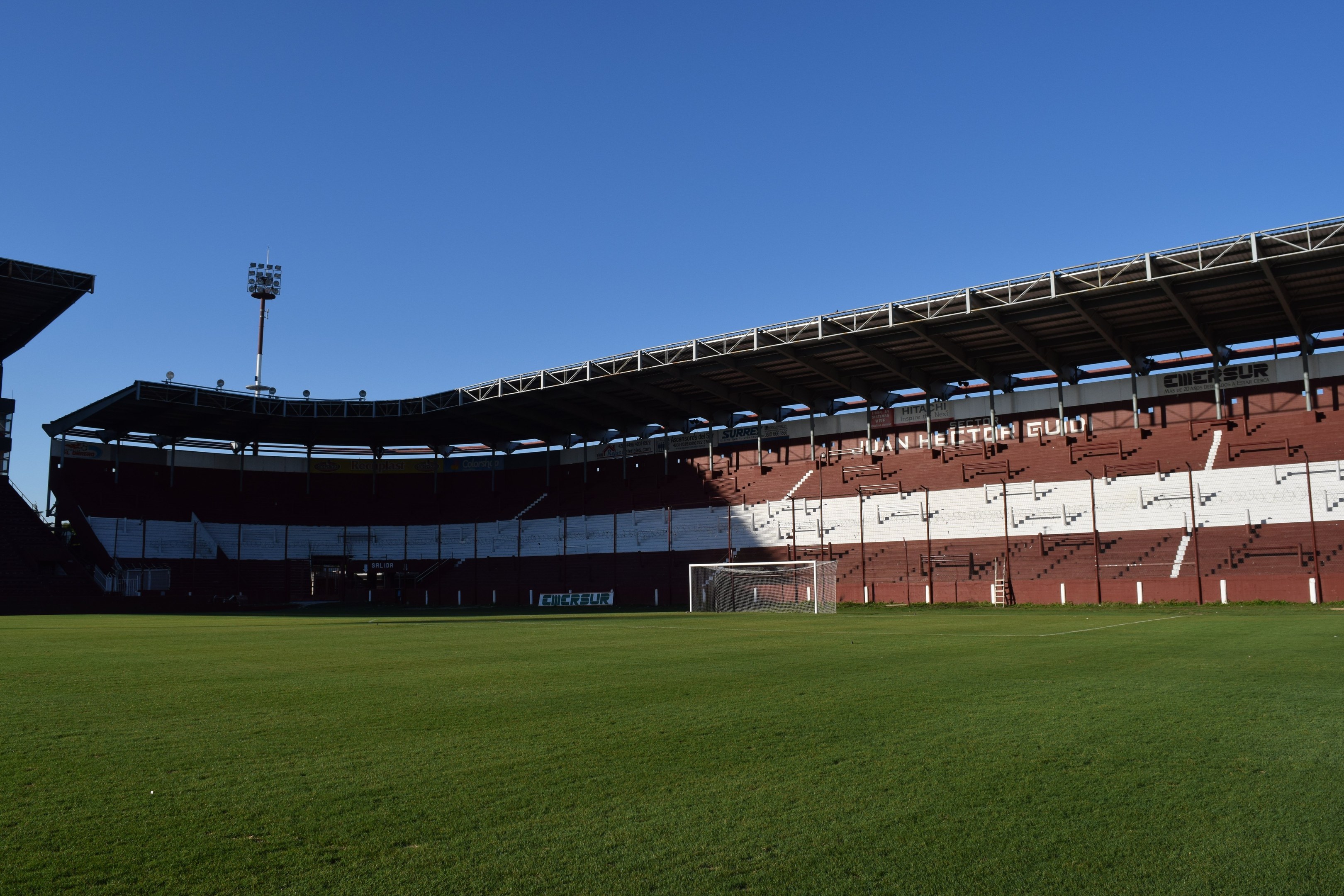Ein Fußballfeld mit grünem Rasen, einem zentralen Torpfosten und einem beleuchteten Stadion im Hintergrund unter einem sichtbaren Himmel.