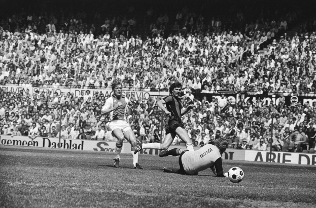 Schwarzes Foto von Männern, die auf einem Feld Fussball spielen, mit Zuschauern im Hintergrund und einer Bundesliga 1978-79 Ajax 1-1 Hannover 96 Fahne.