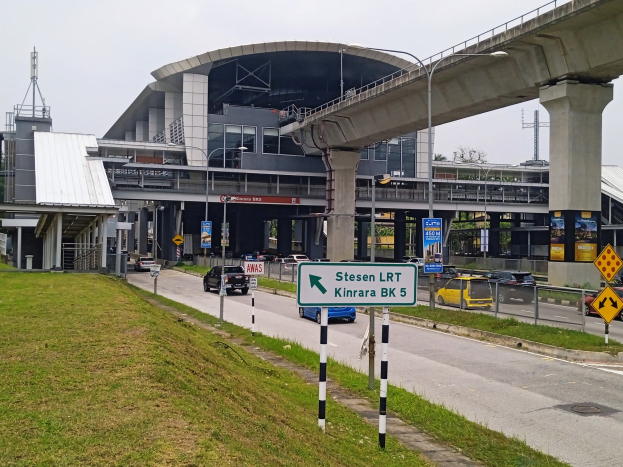 Autobahn mit fahrenden Autos, entfernter Brücke, beleuchtete Straßenlaternen, Schilder an Pfählen, grasbewachsenem Boden, Gebäude mit Säulen, Bäumen und bewölktem Himmel.