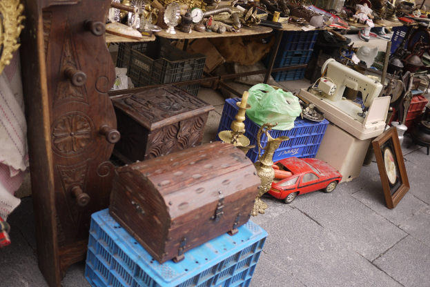 Ein Flohmarktstand mit Holzboxen, einem Spielzeugauto, einer Nähmaschine, einem Foto Rahmen, einer Uhr und anderen Gegenständen auf Tischen.